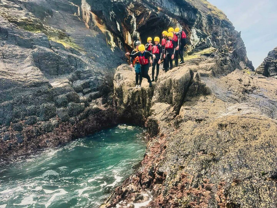 a group of people standing on a cliff side coasteering