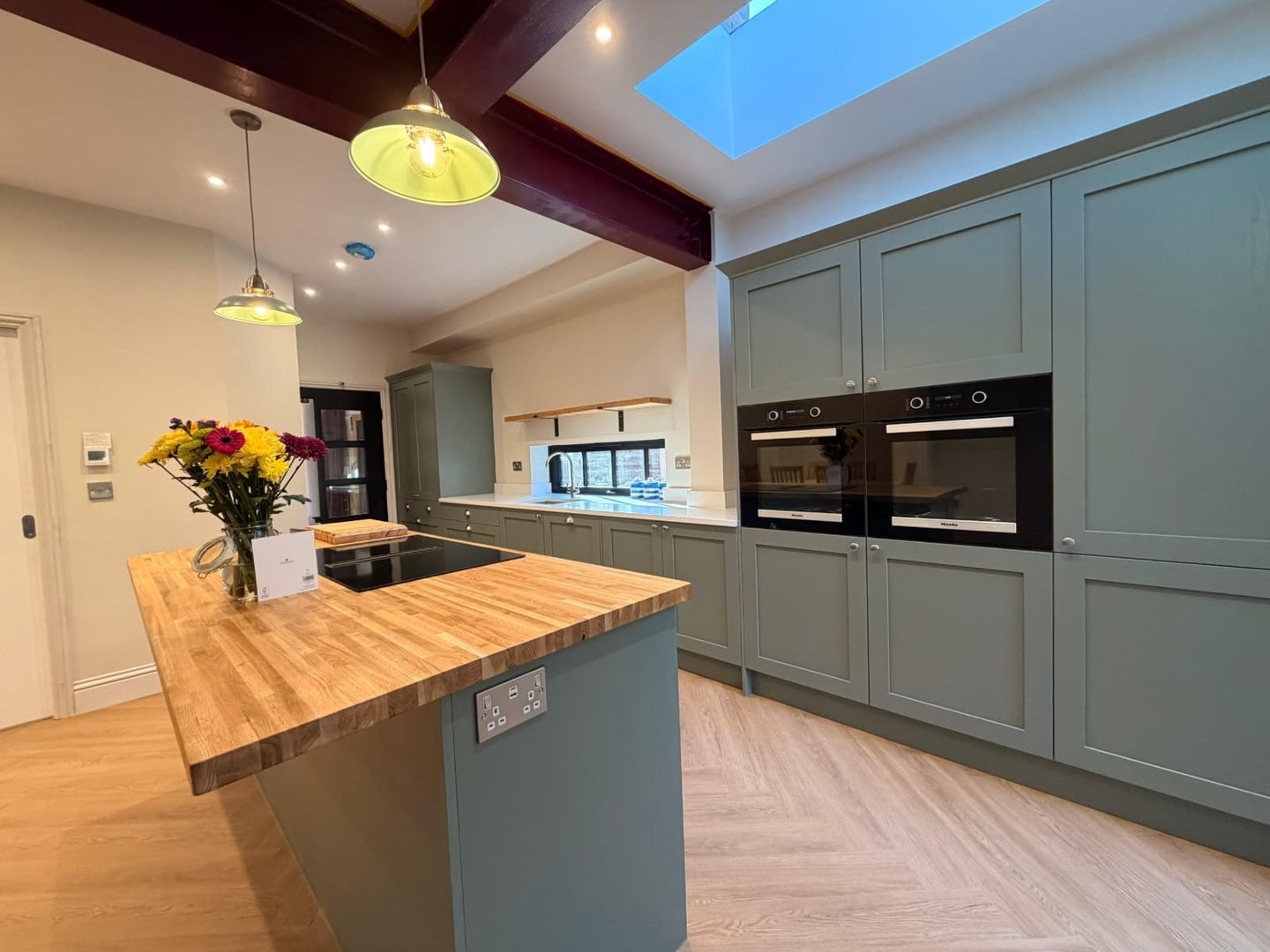 Modern sage green shaker kitchen with wooden butcher block island and integrated double ovens.
