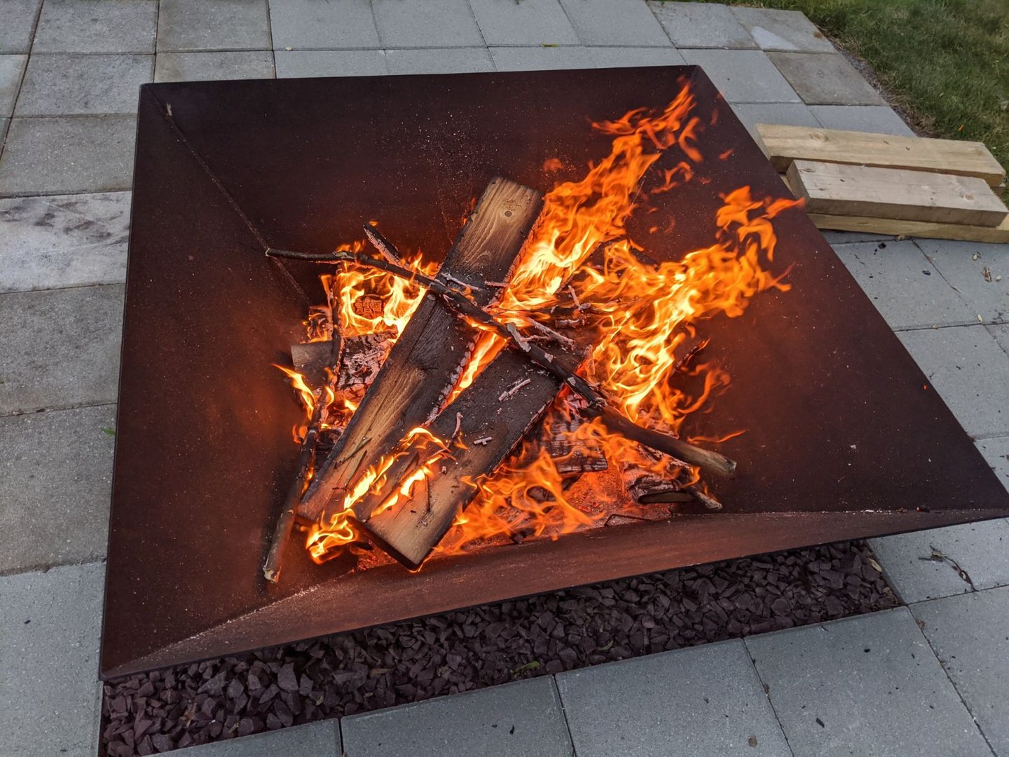 a square steel firepit with a large fire burning inside