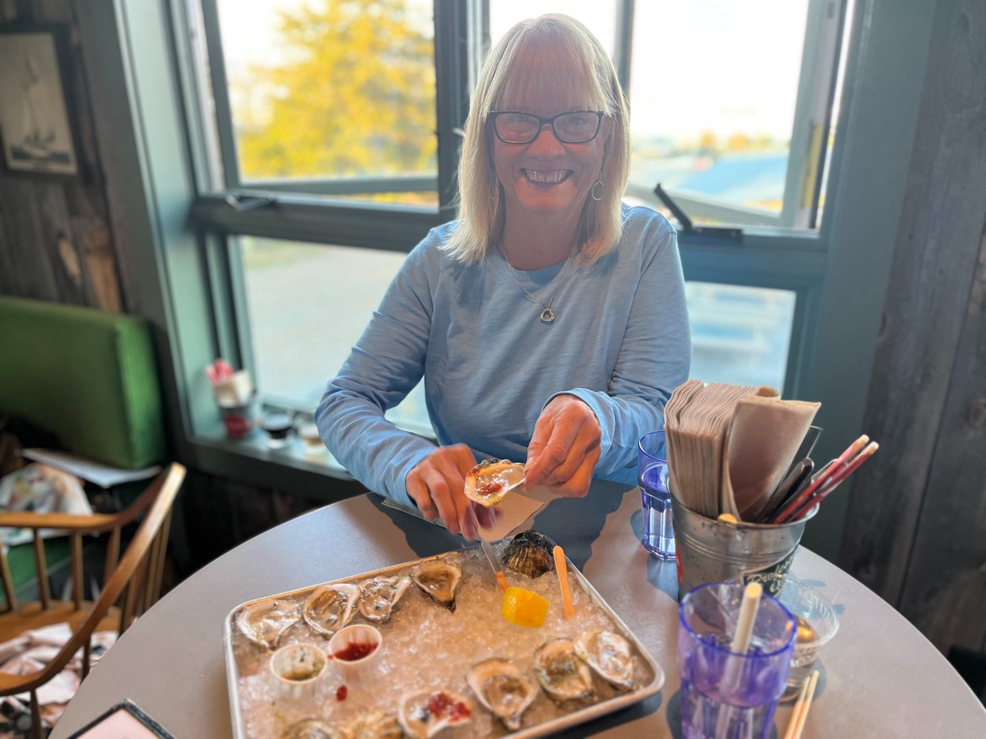 a woman in glasses and a blue shirt is holding a tray of oyster oysters