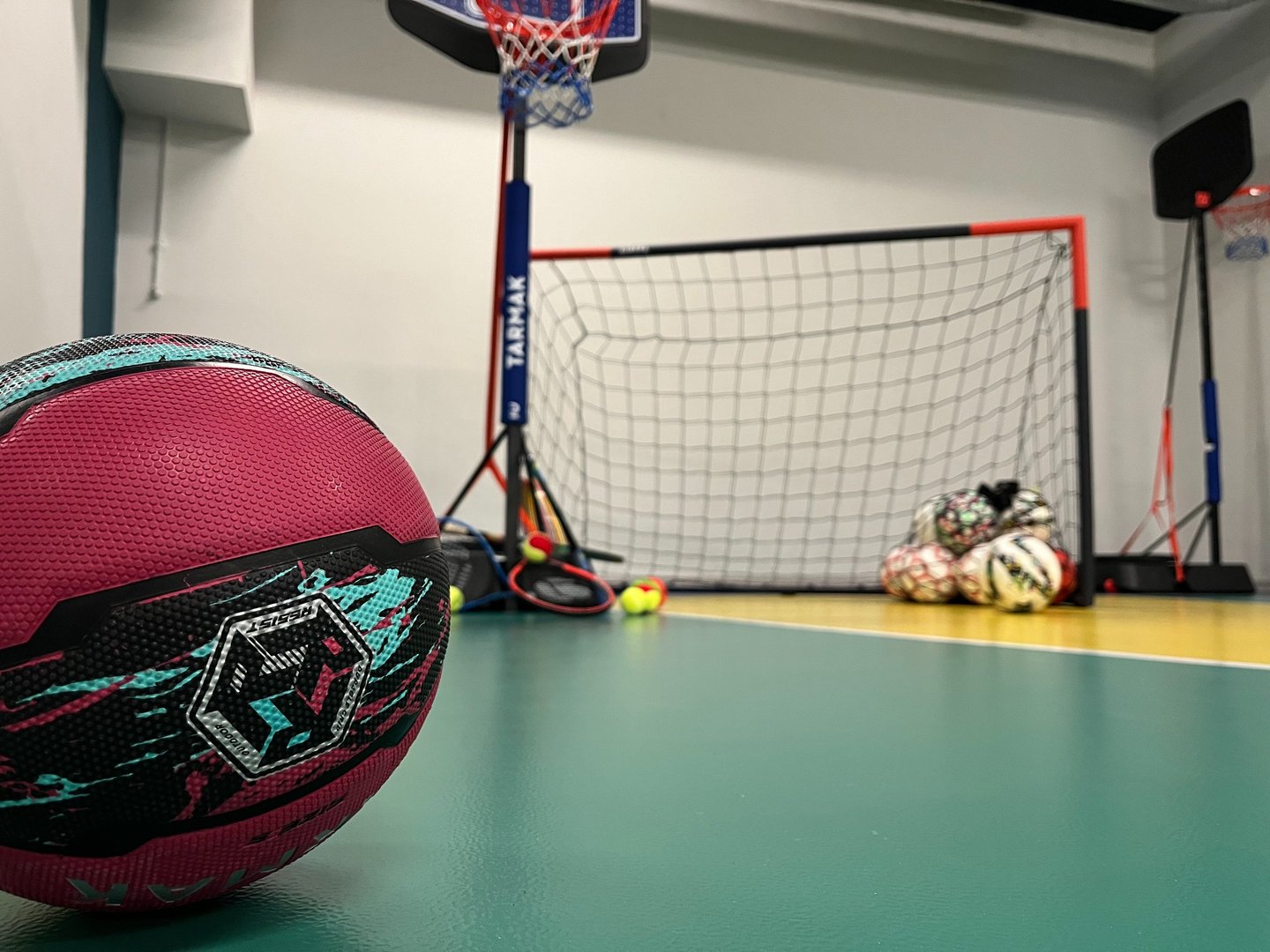 Primo piano di un pallone da basket rosa su un campo multisport nella palestra Move 2 Grow a Milano, con canestro, porta e al