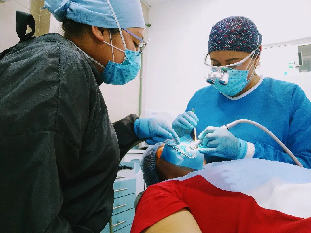 Dentista profesional y asistente realizando una cirugía dental a un paciente en una clínica.