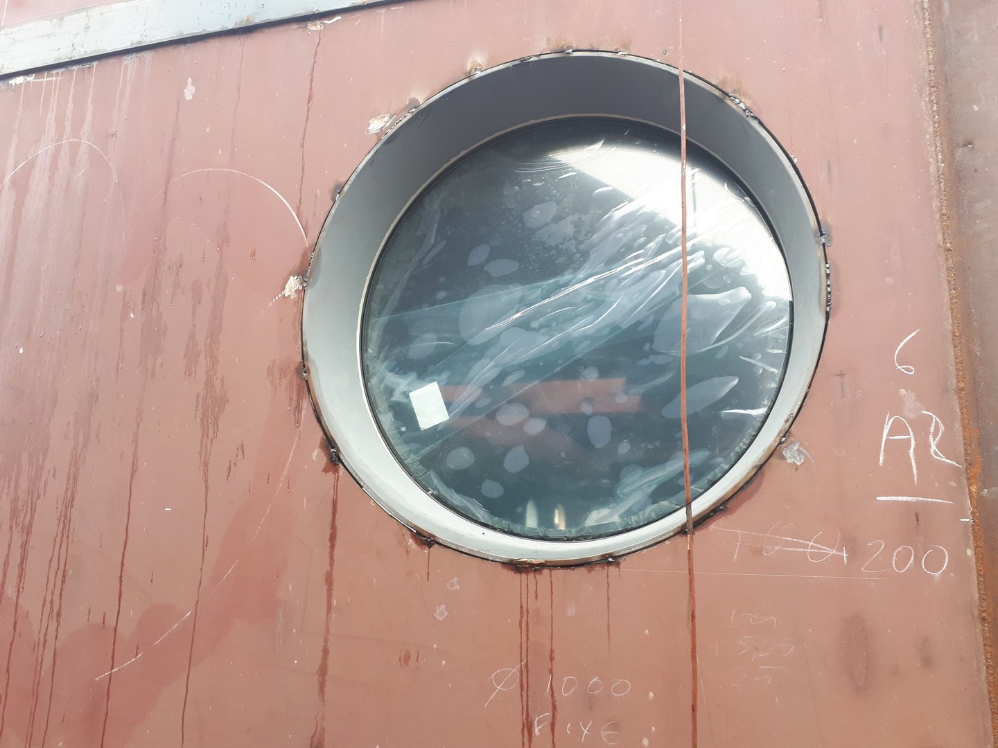 Detailopname van een van onze grote lasbare stalen patrijspoorten gemonteerd op een onbewerkte scheepsromp in aanbouw