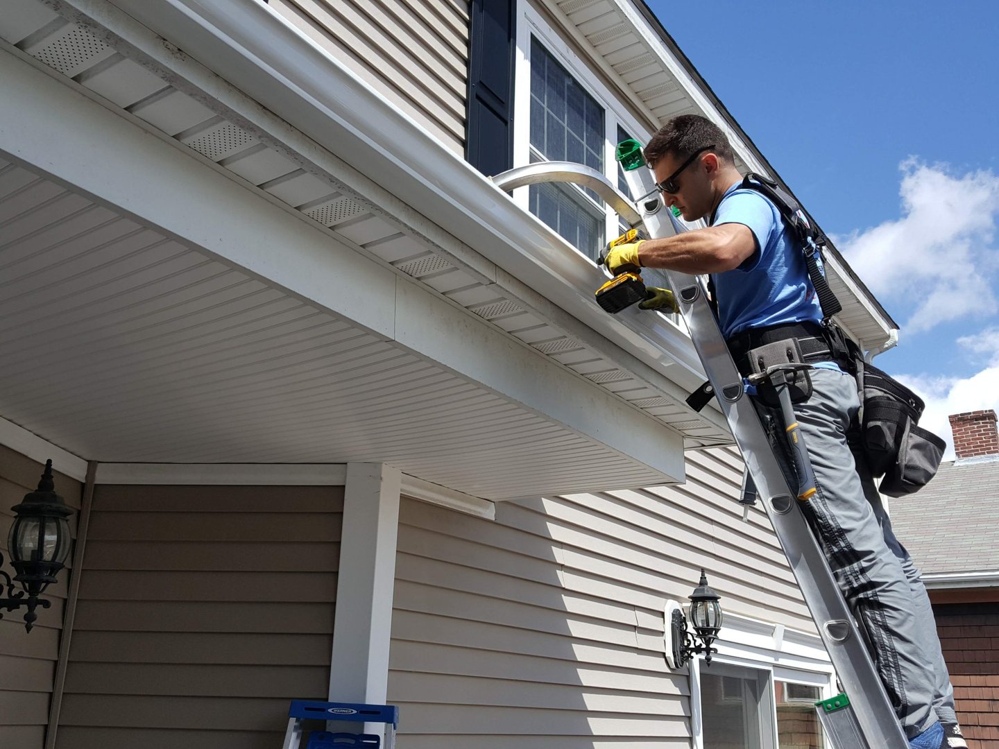 Technician safely positioned on a ladder tightening a heavy-duty gutter bracket with a drill, reside