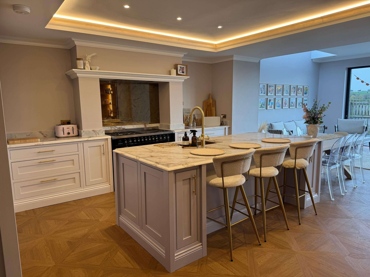 Luxury kitchen with marble island, gold hardware, and bar stools under warm cove lighting.