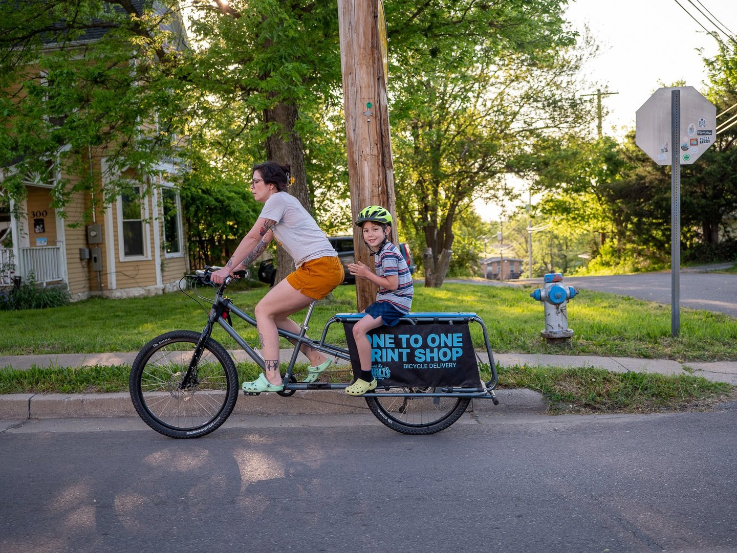 A mother riding her bike with a young boy sitting behind her on a rack