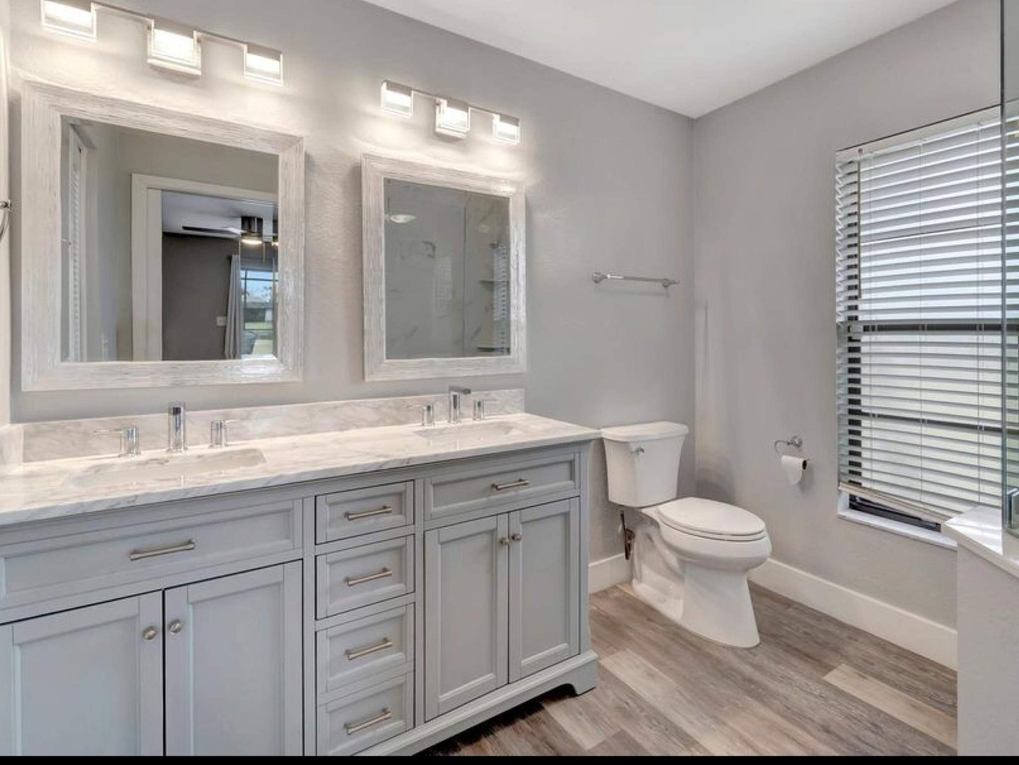Bathroom remodel with a double vanity, framed mirrors, overhead lighting, and a toilet.