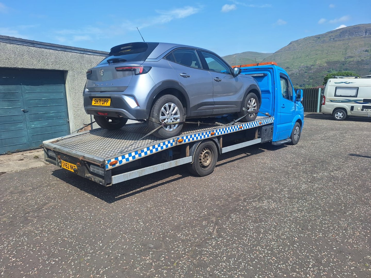 A silver Vauxhall Mokka car being transported on a blue flatbed recovery tow truck.