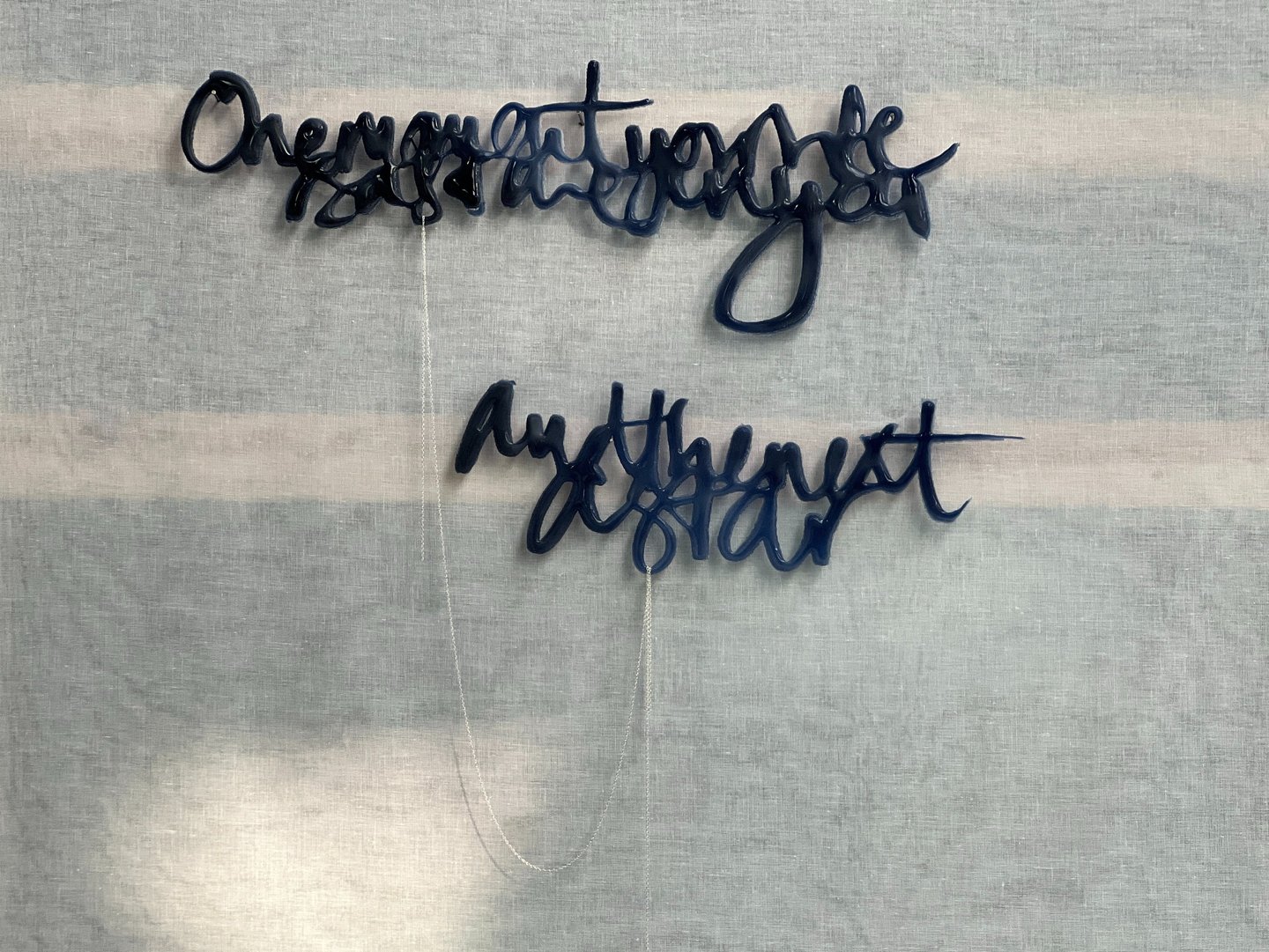 Two lines of semi-abstract text, made in glass and joined by a silver rope chain.