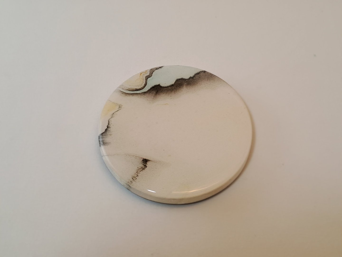 Handmade gypsum coaster with a minimalist white glaze and black marble ink swirl pattern.