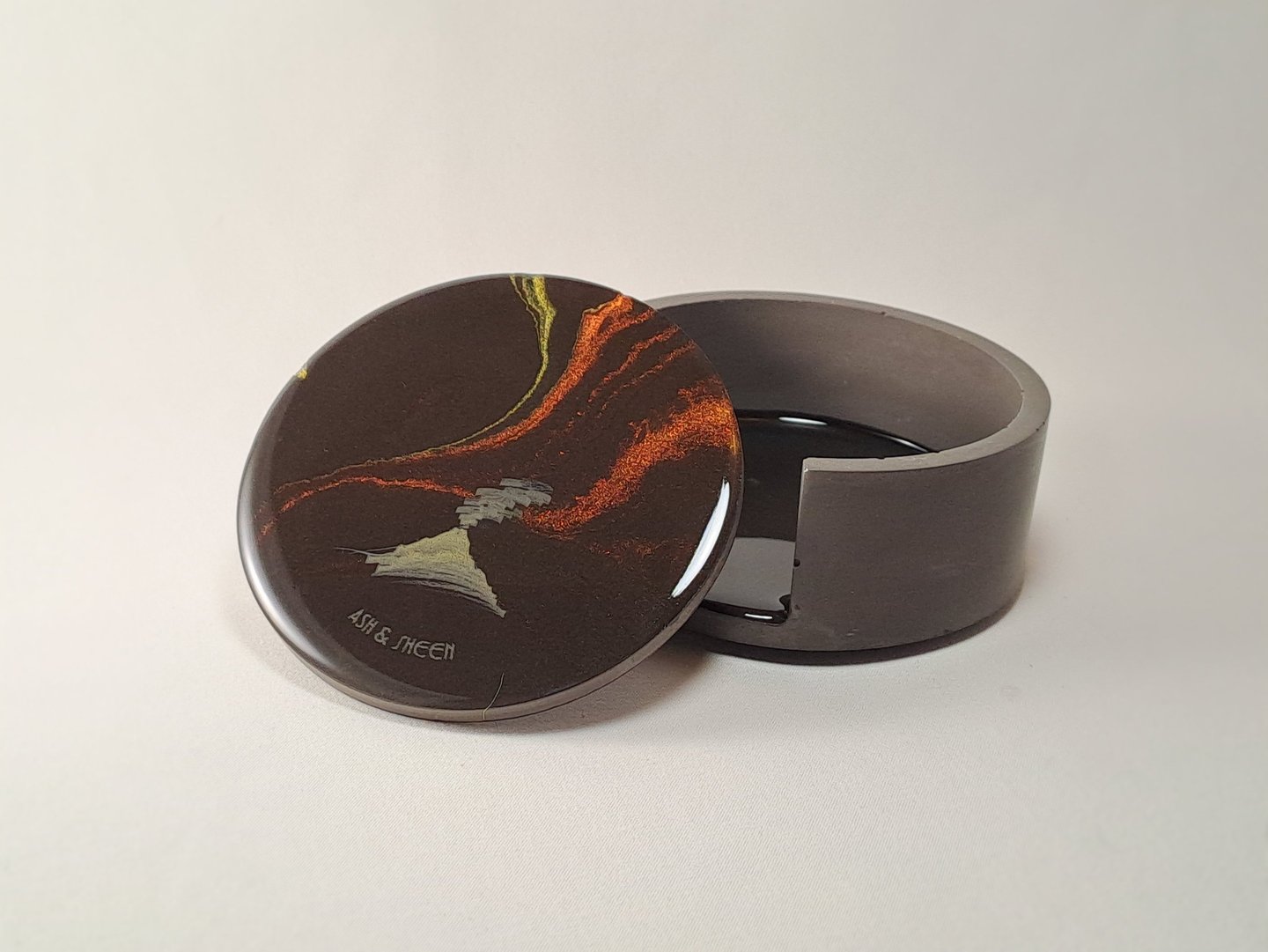 Handmade resin coaster with abstract volcano art resting against a grey gypsum holder.