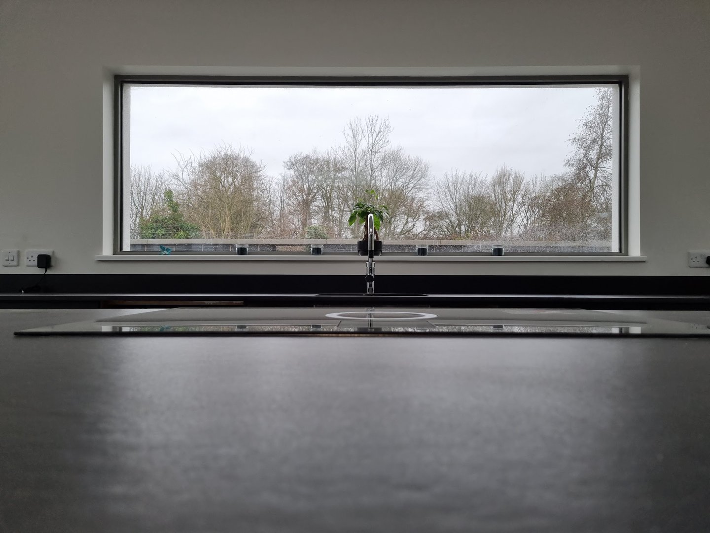 Modern kitchen sink with a chrome faucet in front of a large picture window overlooking a winter forest.