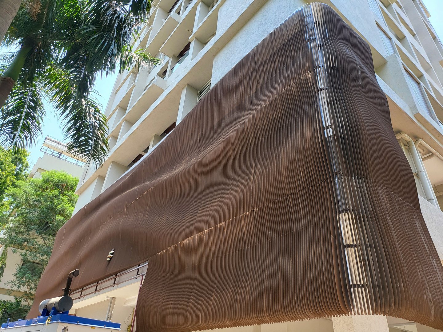 Modern building facade featuring a wavy brown metal architectural screen for sun shading and privacy.