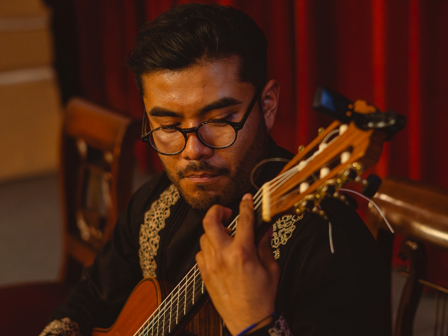A musician wearing glasses plays a classical acoustic guitar during a live performance.