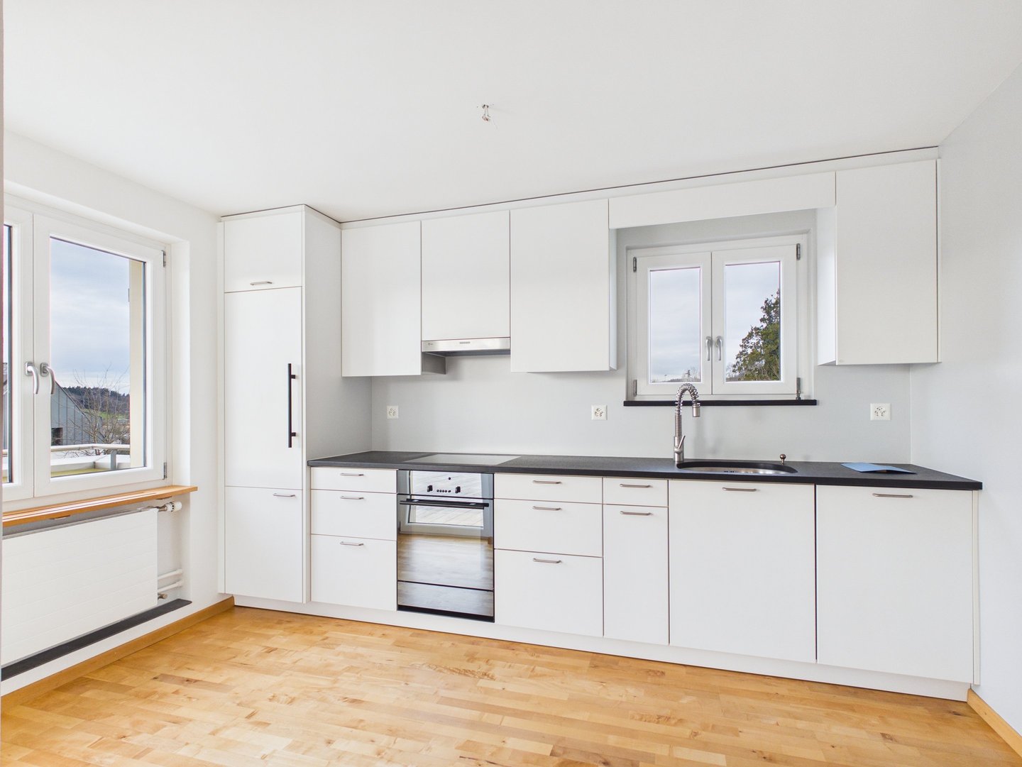 Moderne weiße Küche mit Edelstahlgeräten, schwarzen Arbeitsplatten und hellem Holzboden.