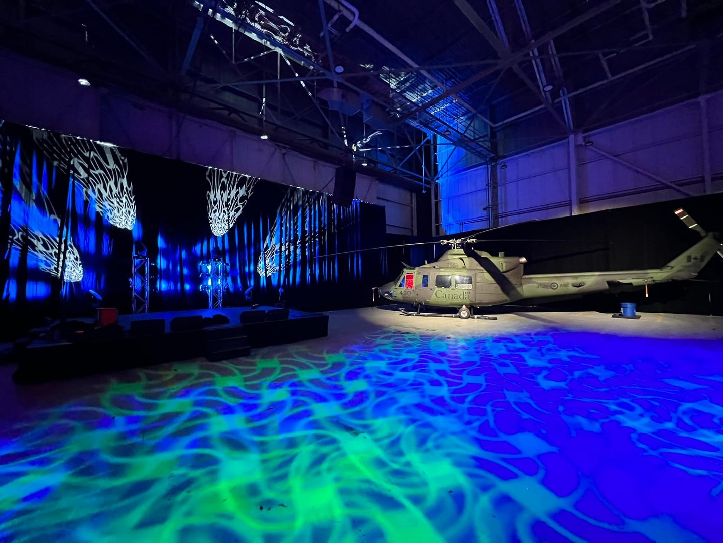 Military helicopter in a hangar with dramatic blue and green stage lighting and projections.