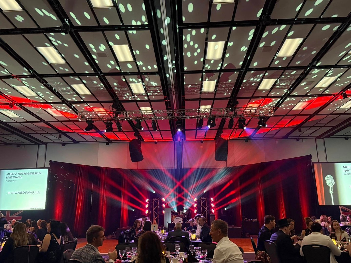 A corporate gala event featuring red stage lighting, spotlights, and guests seated at banquet tables.