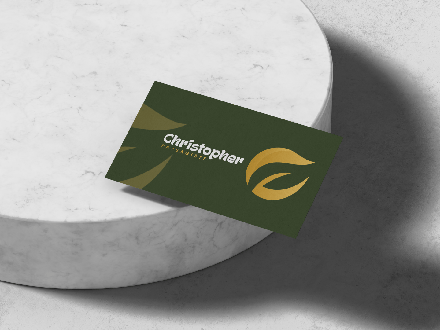 Carte de visite verte pour paysagiste avec logo en feuille d'or sur un piédestal en marbre blanc.