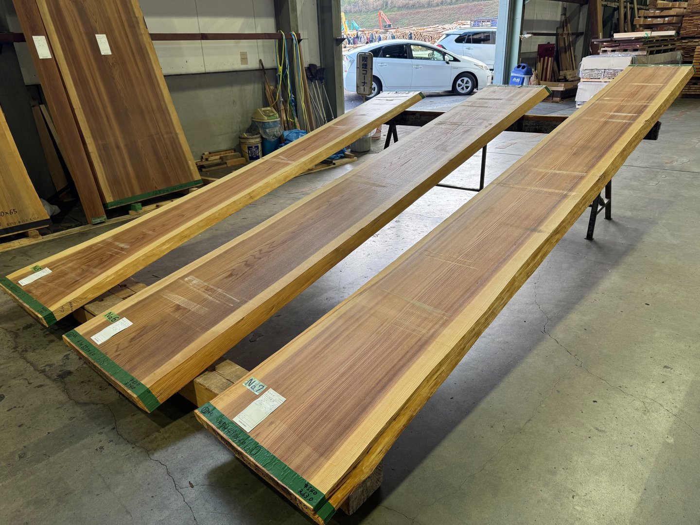 Three long, natural edge raw wood slabs displayed in a lumber mill for custom furniture making.