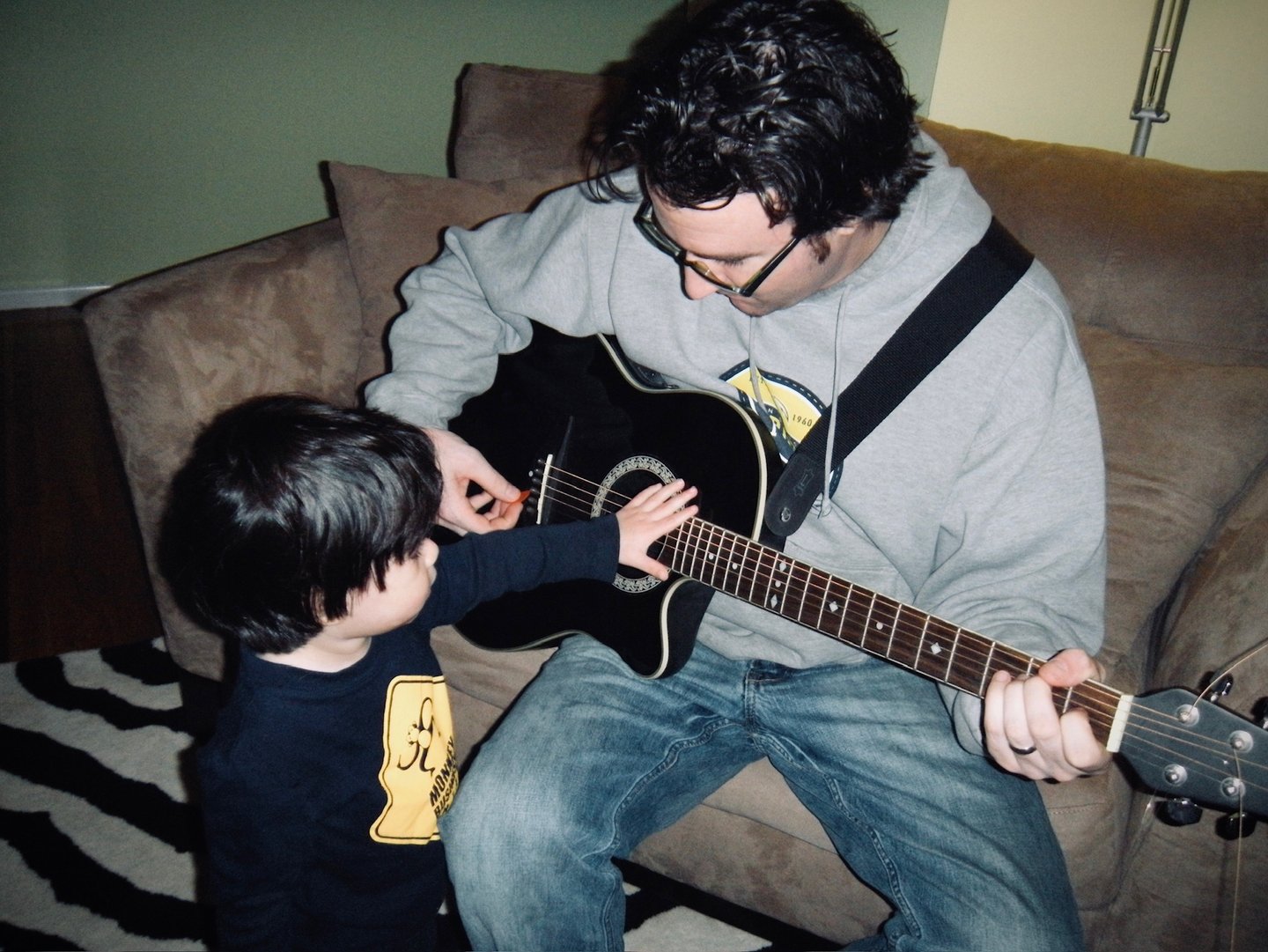 A father sitting while playing guitar with his toddler