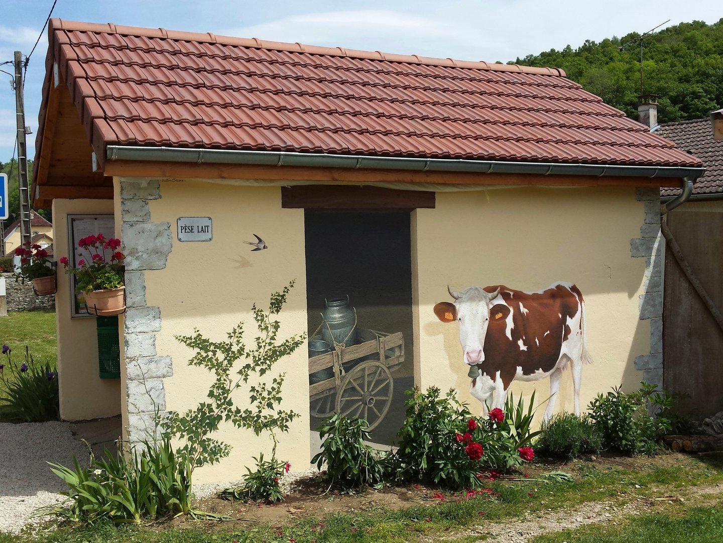 Fresque murale sur façade comporte une fausse porte, une vache et un lierre peints.