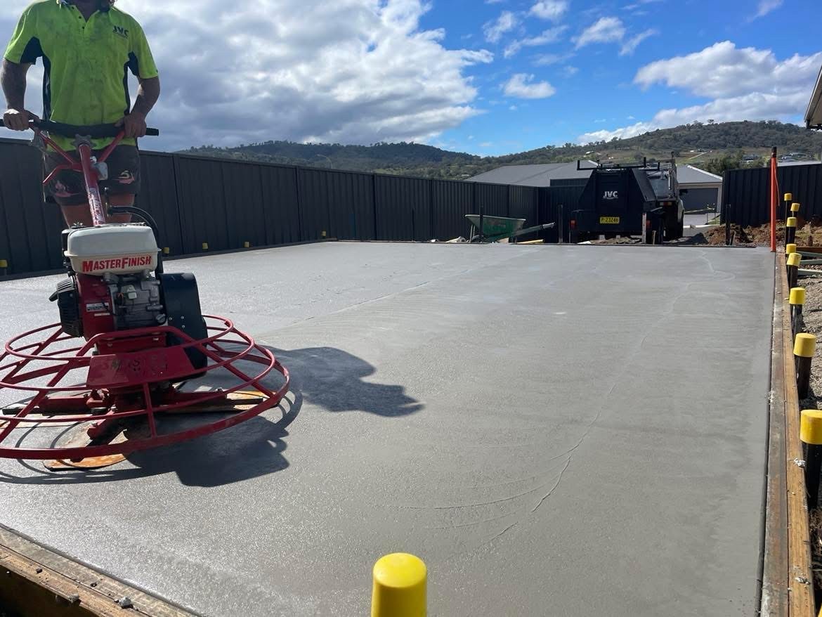 Professional concreter using a power trowel machine to finish a fresh concrete slab for a backyard patio.