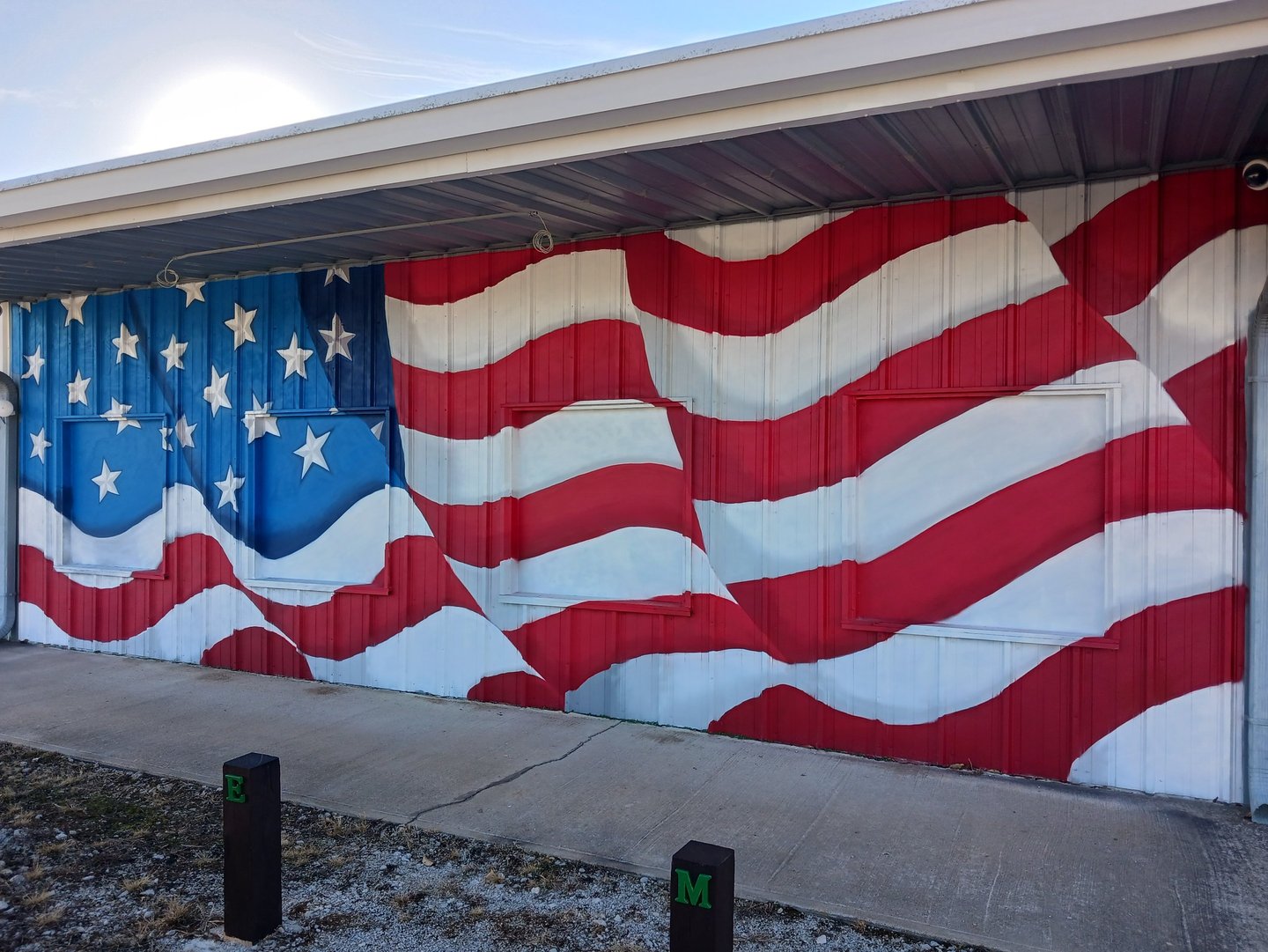 A metal building exterior featuring a patriotic American flag mural with red and white stripes and white stars.
