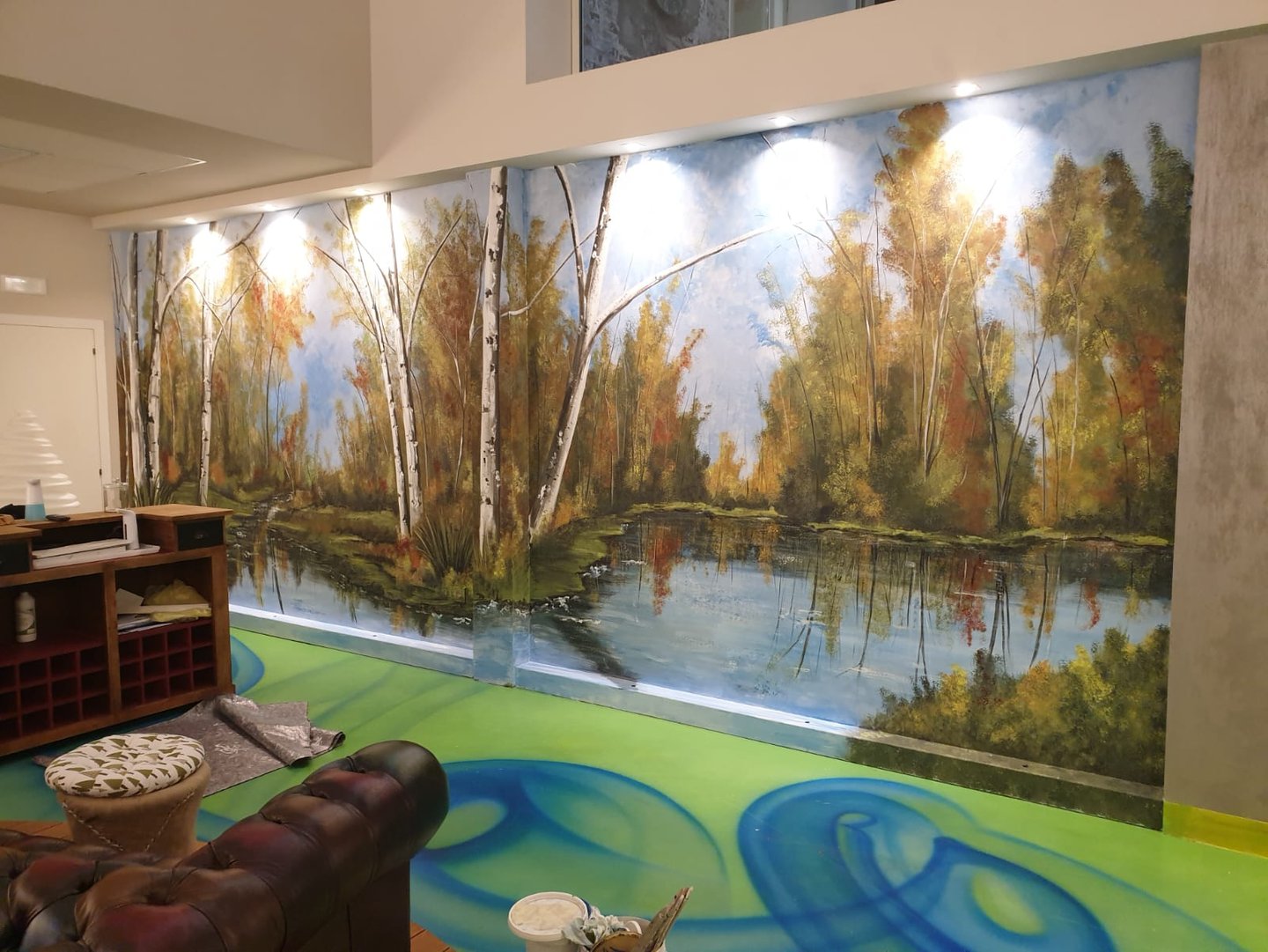 Quadro murale dipinto a mano con lago nel bosco e betulle su una parete interna.