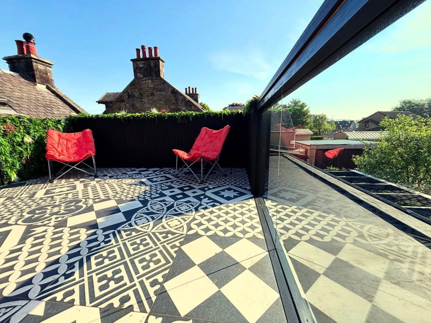 Modern rooftop terrace featuring patterned monochromatic floor tiles and two red folding chairs under a clear blue sky.