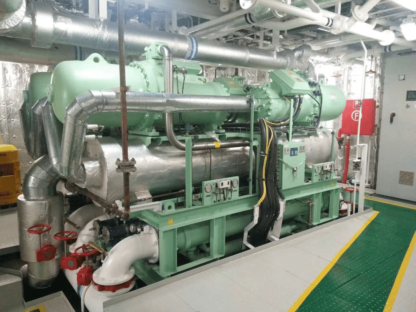 Industrial HVAC water-cooled screw chiller system in a ships plant room with insulated piping.