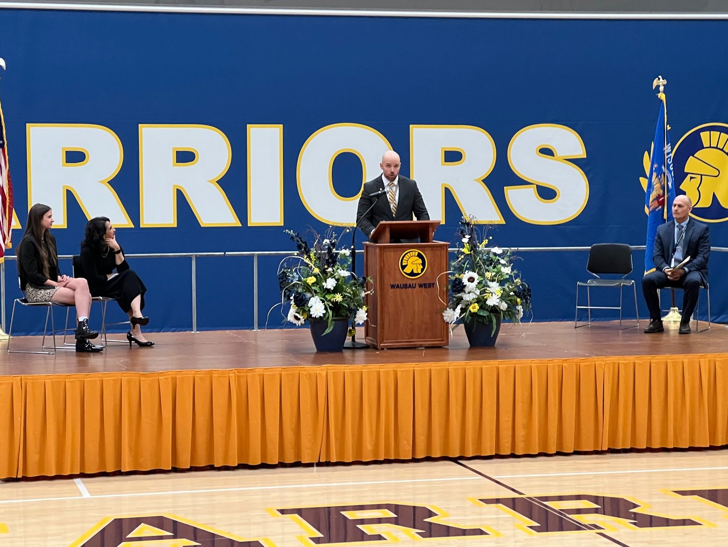 a man standing at a podium with a microphone and a woman sitting at a podium