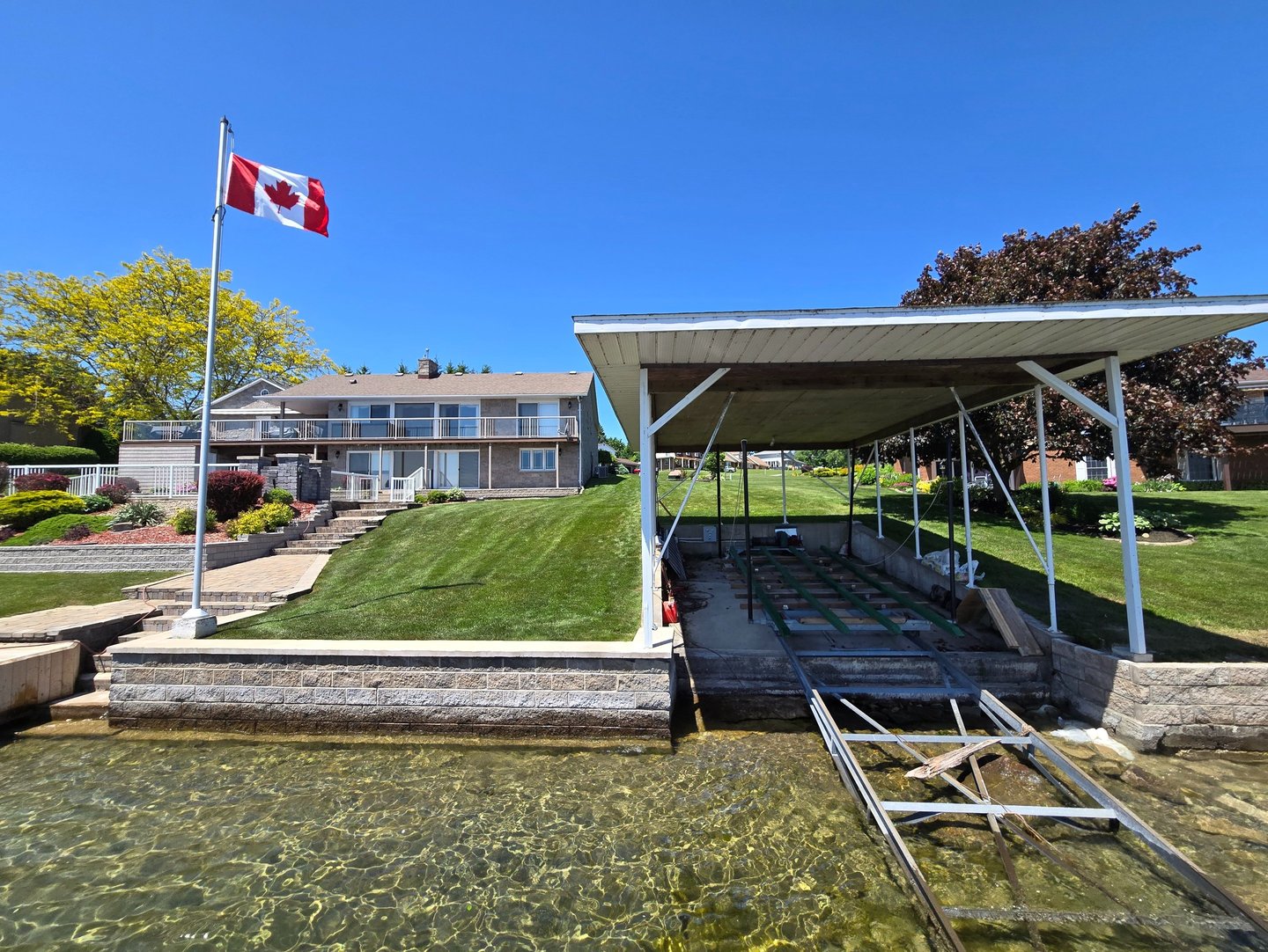 Waterfront cottage in Canada with a boat lift, private dock, and Canadian flag under a clear blue sky.