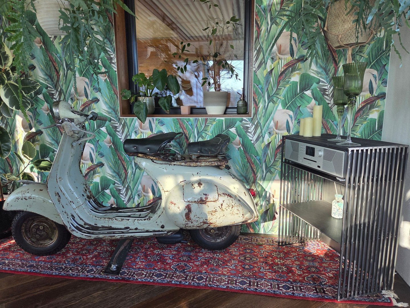Vintage-Vespa als dekoratives Highlight vor Dschungel-Tapete neben modernem Holz-Sideboard.