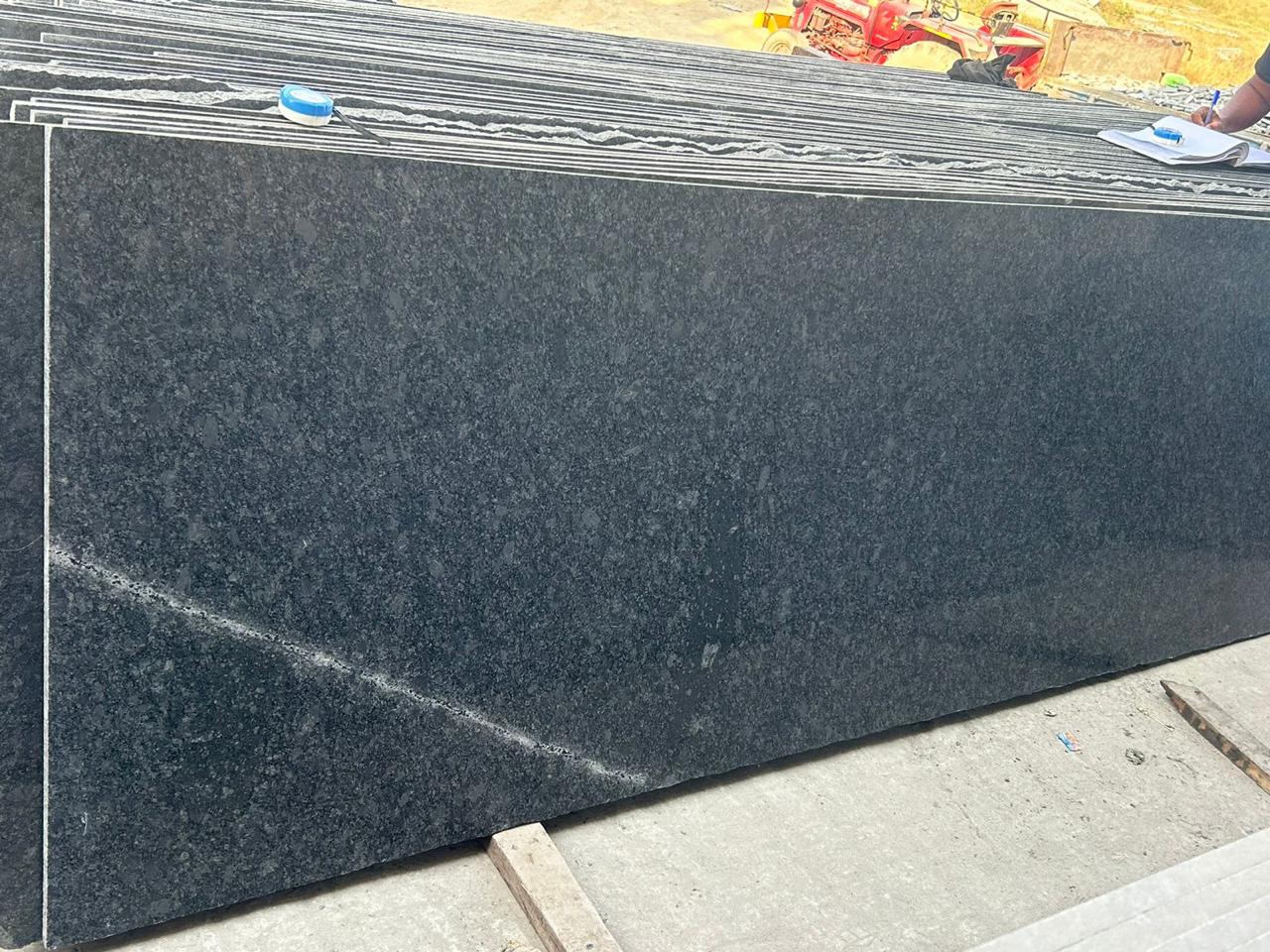 Polished black granite slabs stacked outdoors for kitchen countertops and flooring installation.