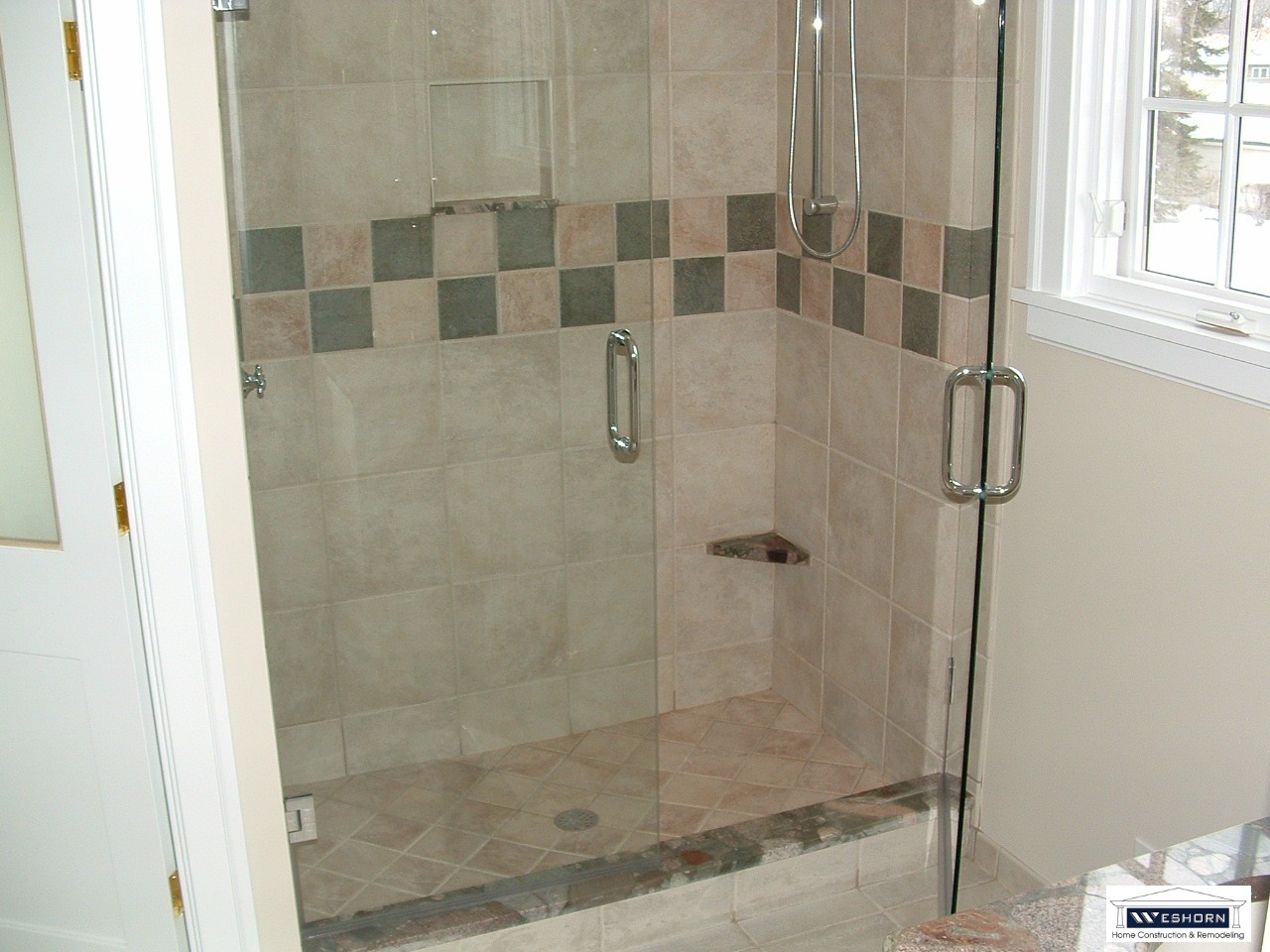 Walk-in shower featuring glass doors, neutral porcelain tiling, and a decorative mosaic border.