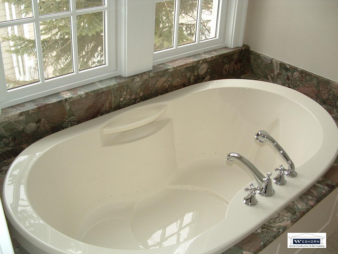 Luxury oval soaking tub with chrome fixtures and granite tile surround in a modern bathroom remodel.