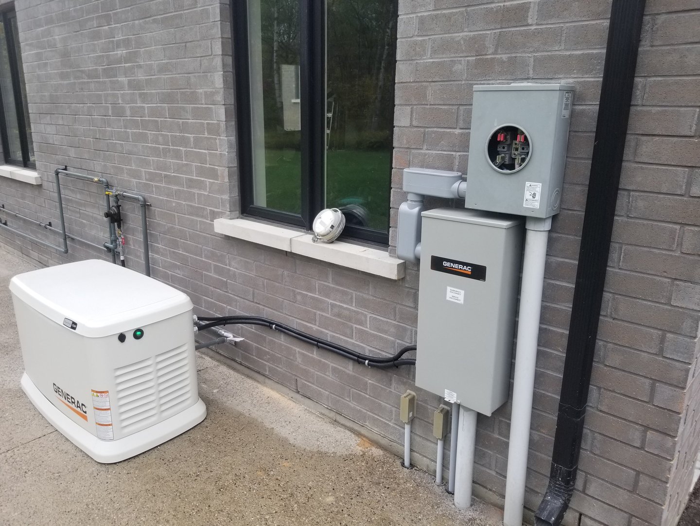 A white Generac standby home generator installed outside a grey brick house next to electrical boxes.