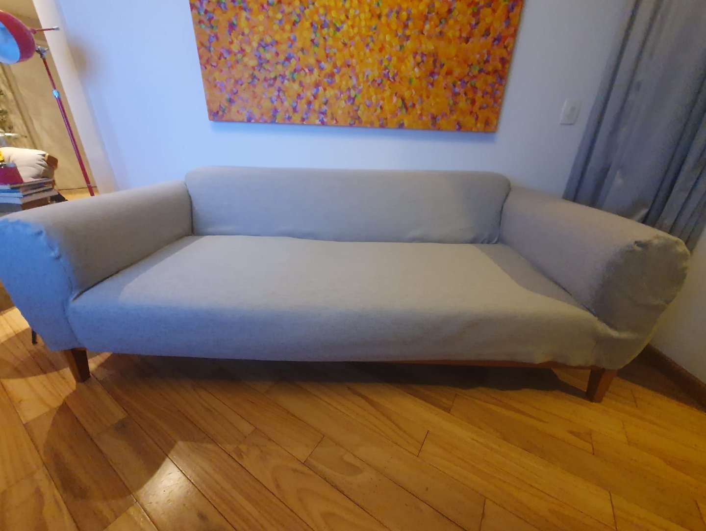 Um sofá moderno de tecido cinza com pernas de madeira em um piso de madeira abaixo de uma pintura ab