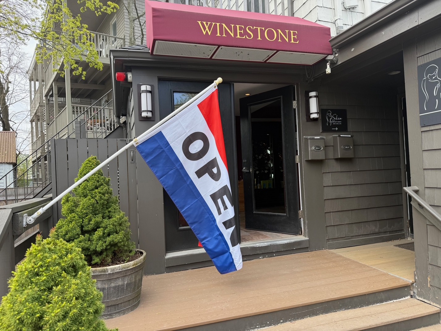 Winestone boutique storefront with a red awning and a tricolor open flag hanging at the entrance.