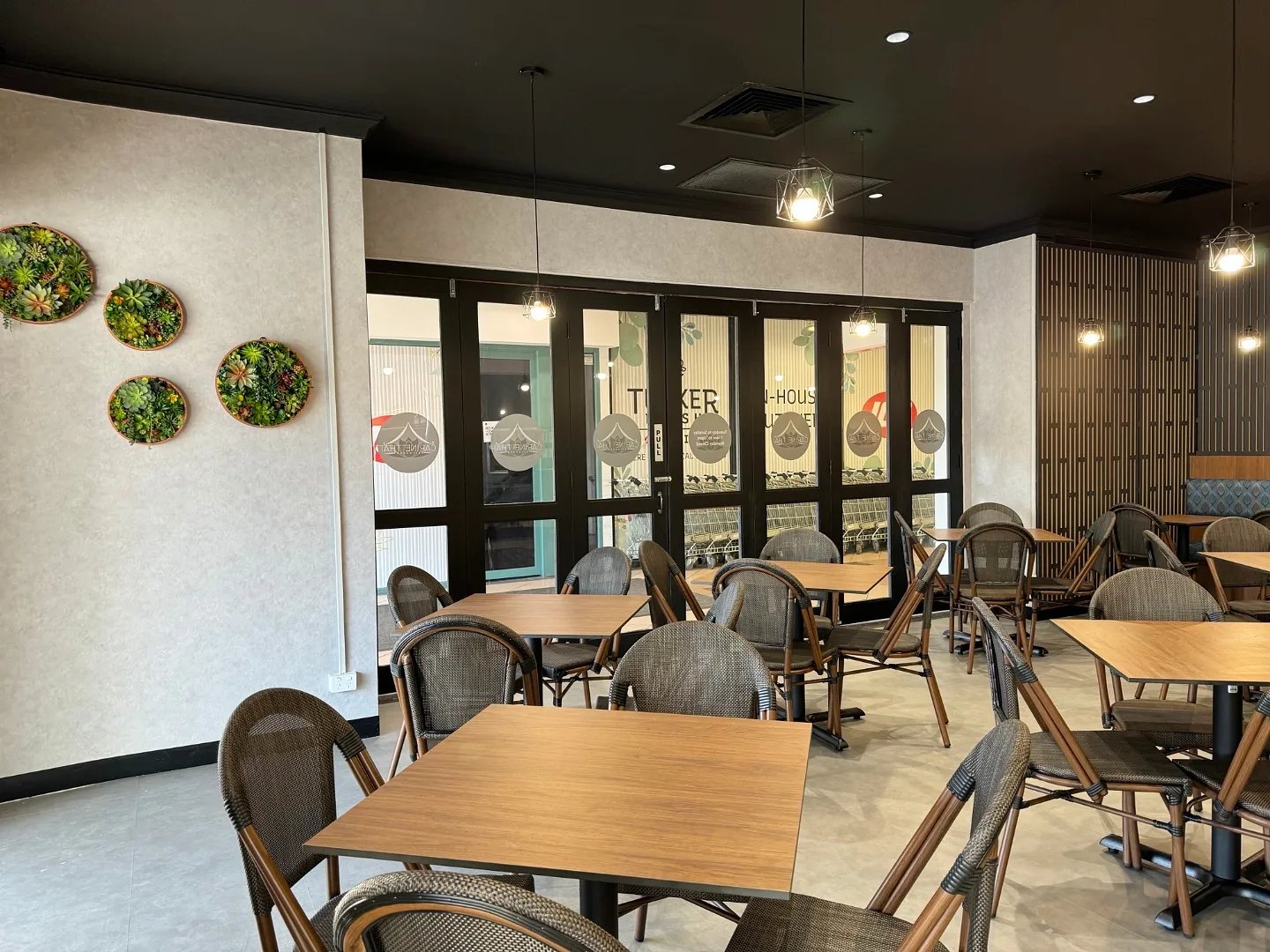 Modern cafe interior with wooden tables, woven chairs, and decorative wall succulents.