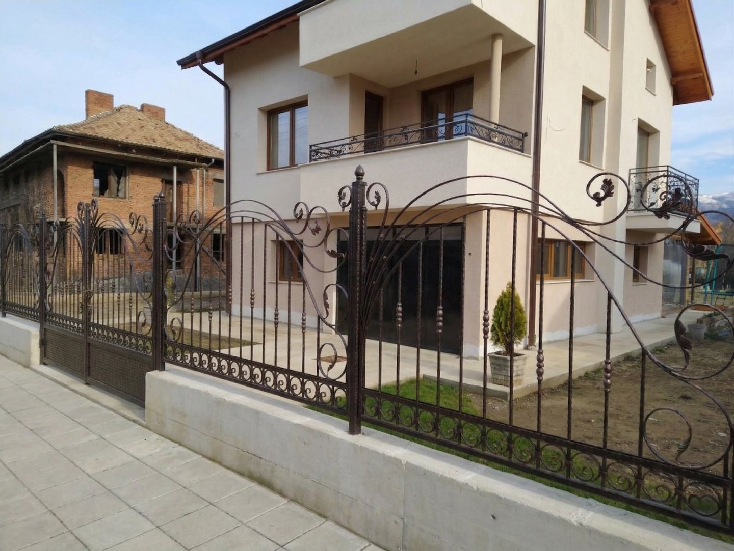 Custom decorative wrought iron fence and gate surrounding a modern two-story residential house.