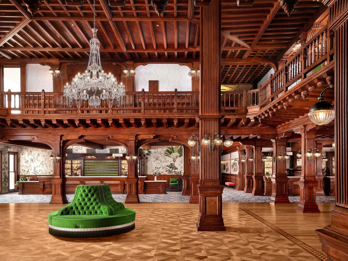 Luxurious hotel lobby featuring ornate wood paneling, a crystal chandelier, and a green velvet circular sofa.