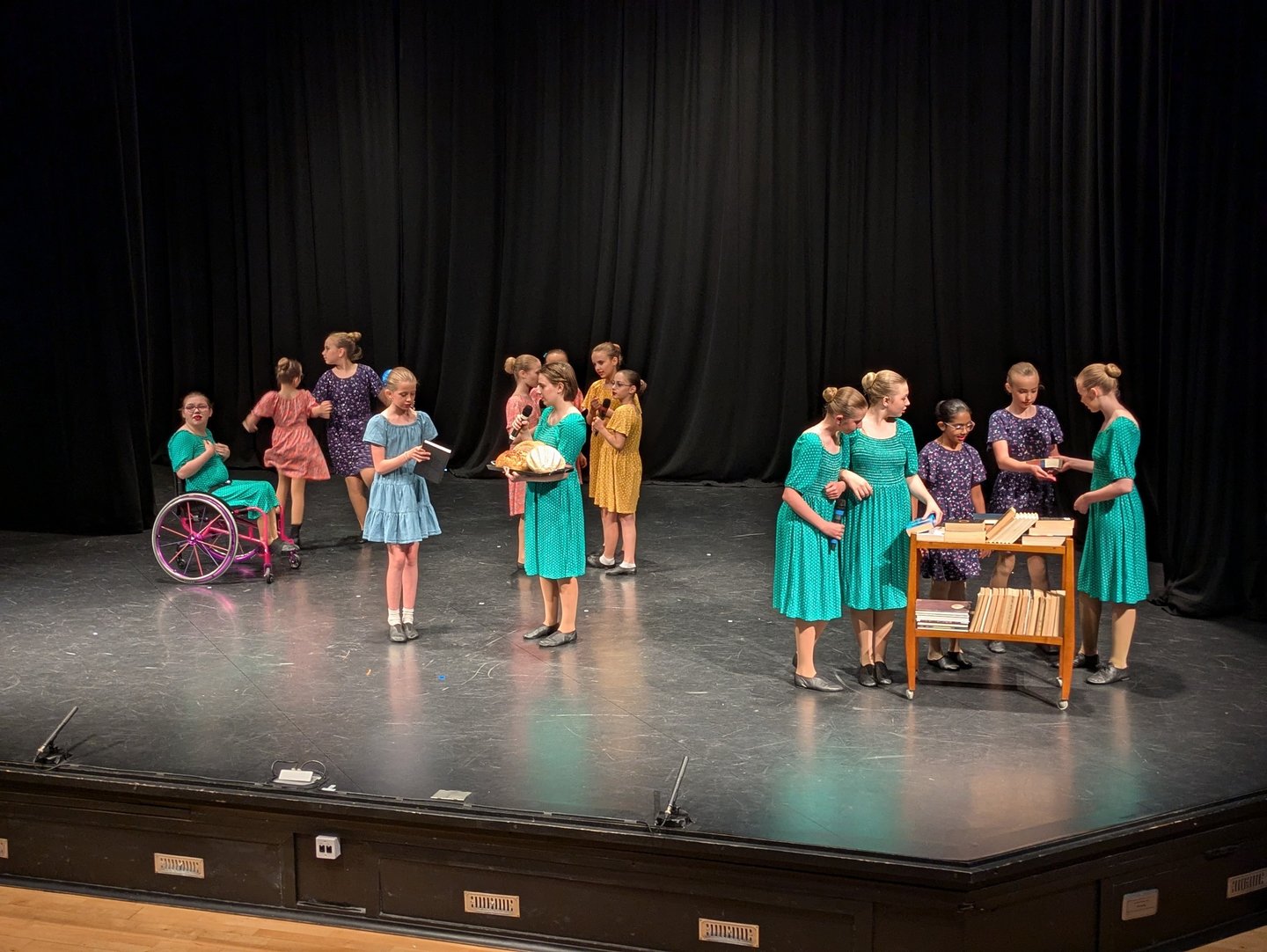 Young girls perform a musical theatre song and drama piece on stage in coloured dresses