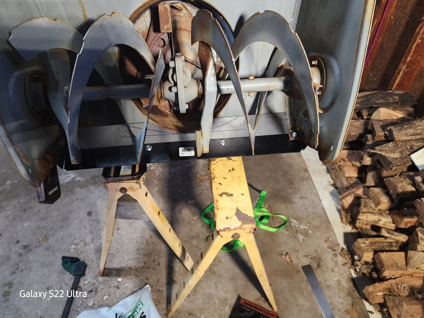 A metal snowblower auger blade assembly mounted on yellow jack stands for winter equipment maintenance.