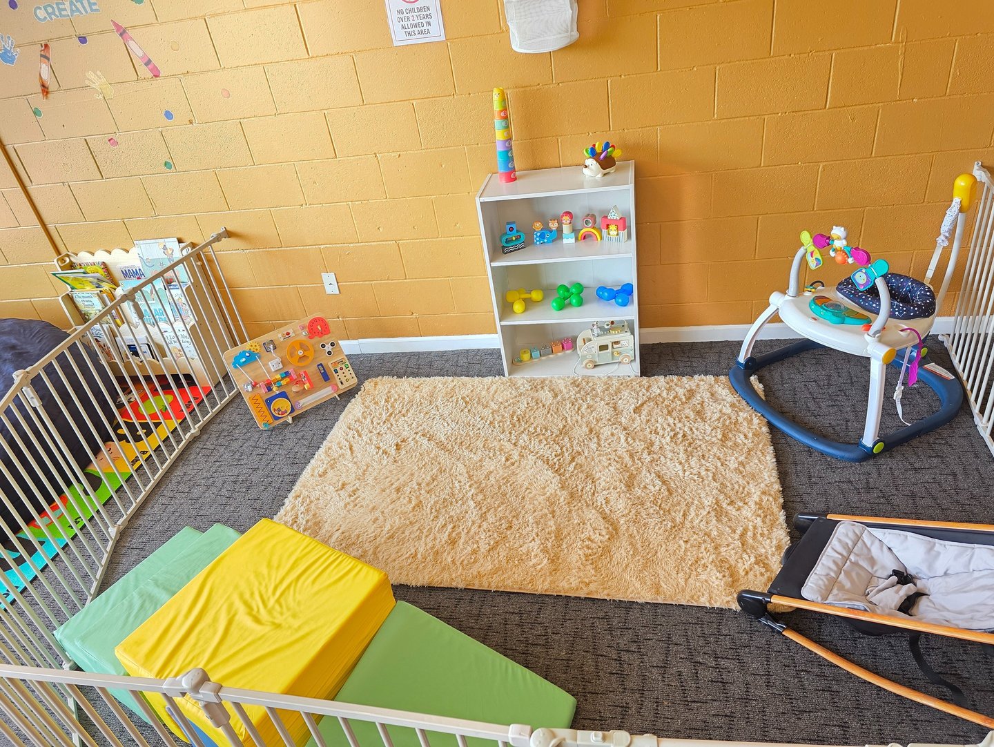 An infant play area with educational silicone and wooden toys, a soft rug, and foam climbing blocks.