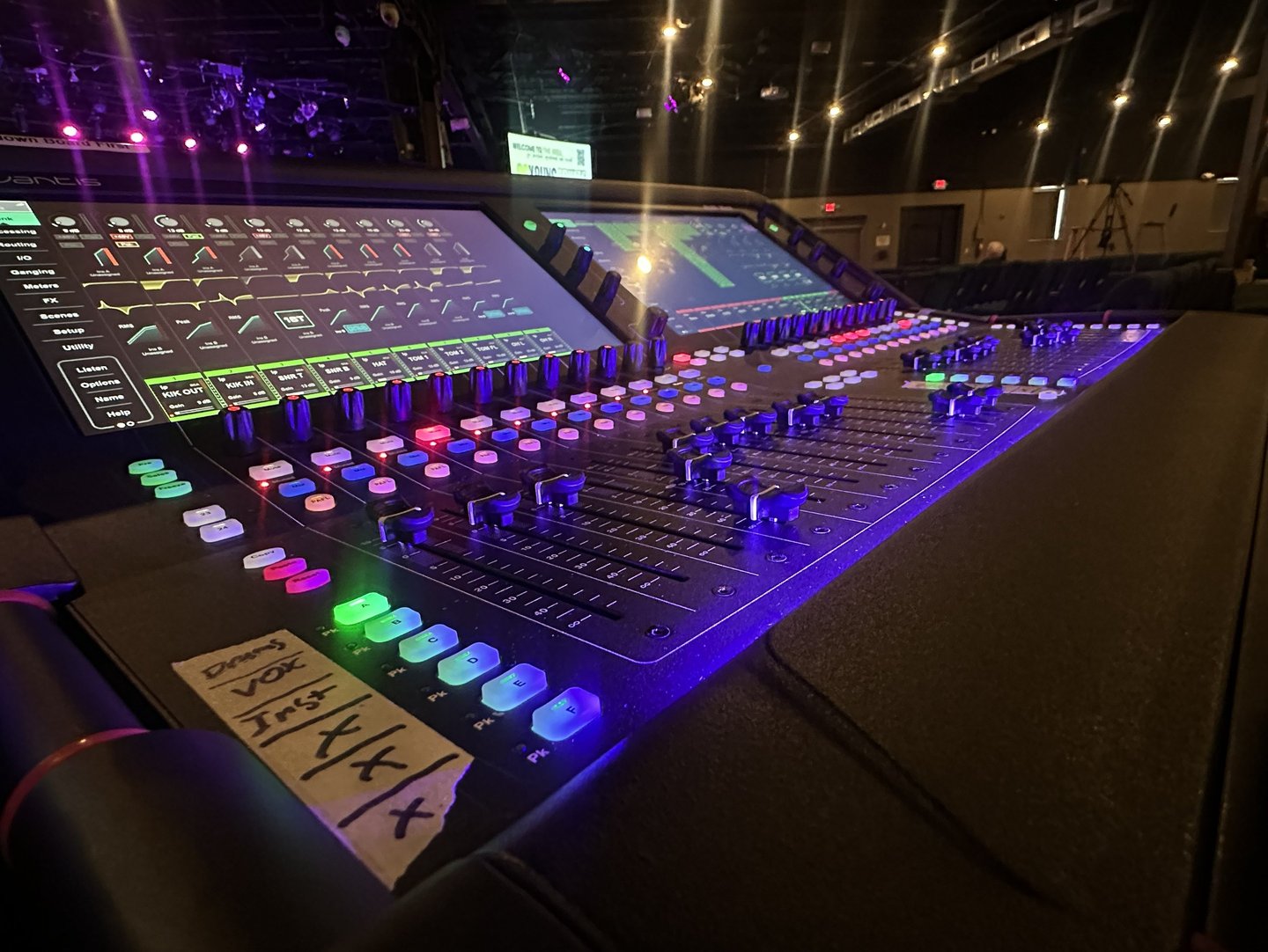 Professional digital audio mixing console with glowing LED buttons and faders in a dark concert venue.