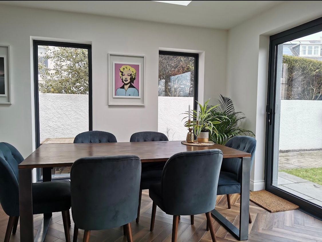 Modern dining room with a wooden table, blue velvet chairs, and pop art on a white wall.