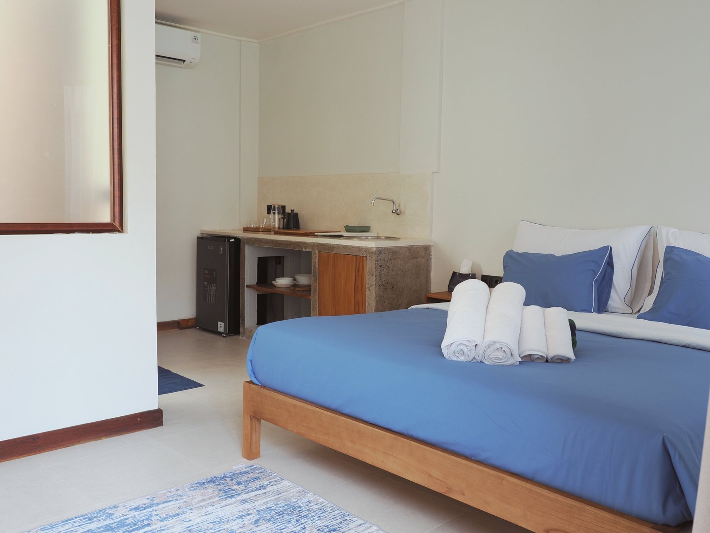 Modern hotel studio apartment featuring a queen bed with blue linens and a compact kitchenette.