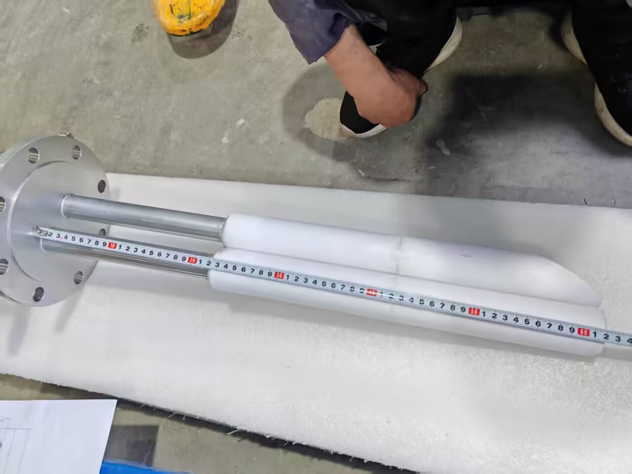Industrial immersion heater with protective ceramic sleeves being measured with a tape rule.