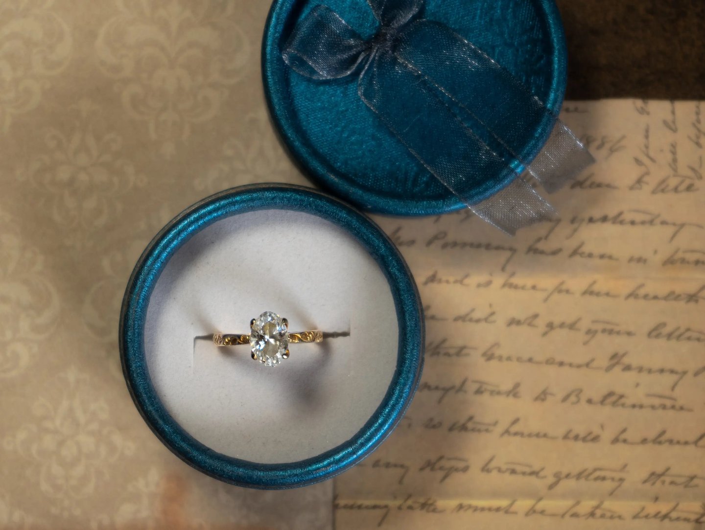 Gold engagement ring displayed in an open teal velvet ring box